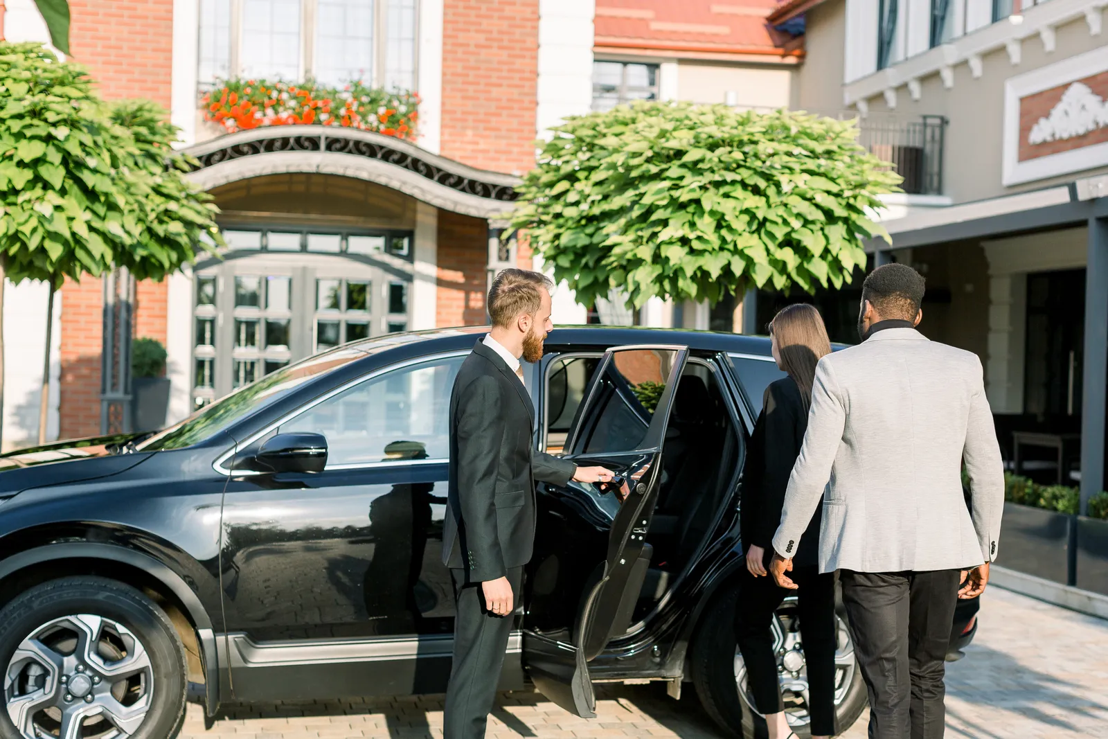 Chauffeur opening the car door for business travellers departing from their address
