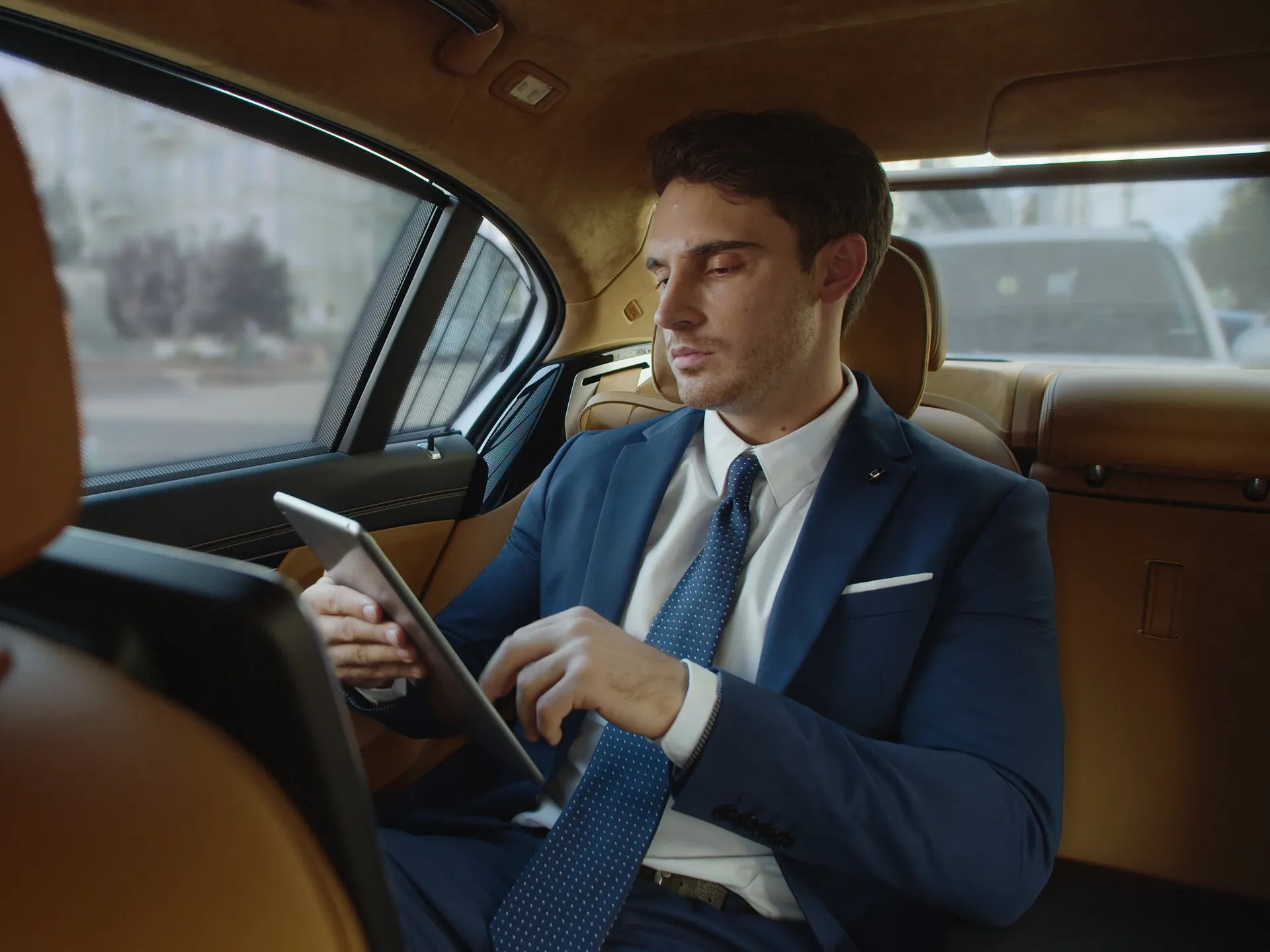 A businessman working on a tablet in the rear cabin of a chauffeur-driven luxury saloon