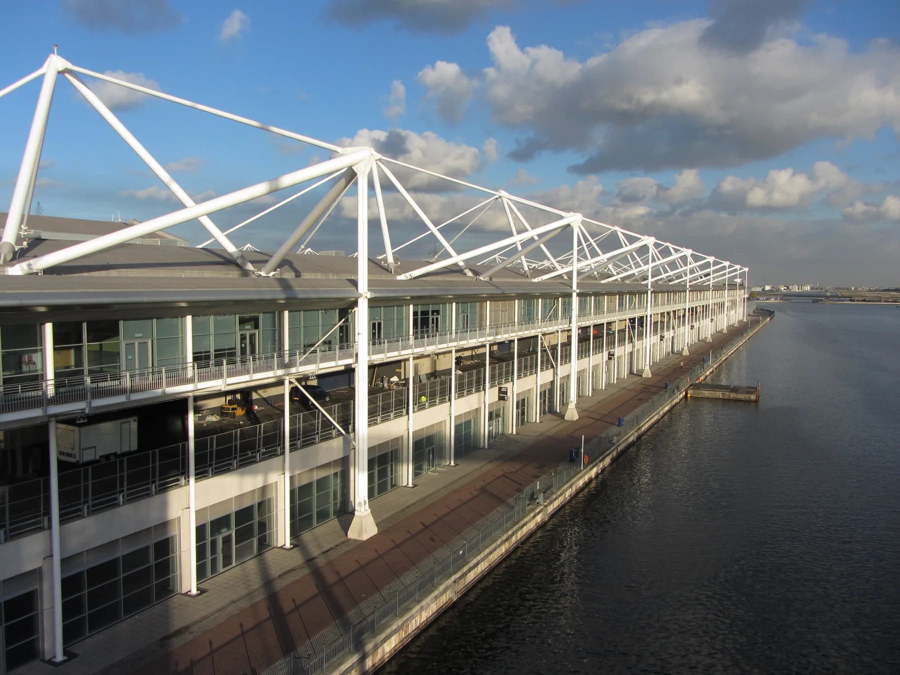 ExCeL London exhibition centre along Royal Victoria Dock, its white mast-and-cable roof structure beside the water