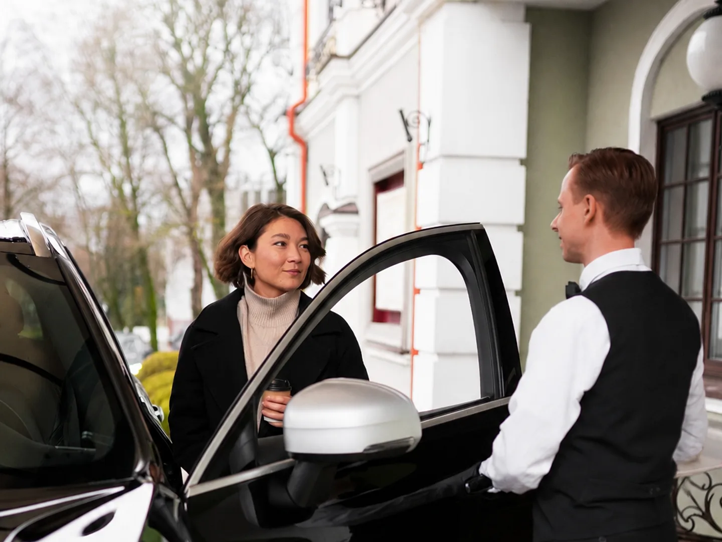 A chauffeur opening the car door for a guest outside an elegant hotel