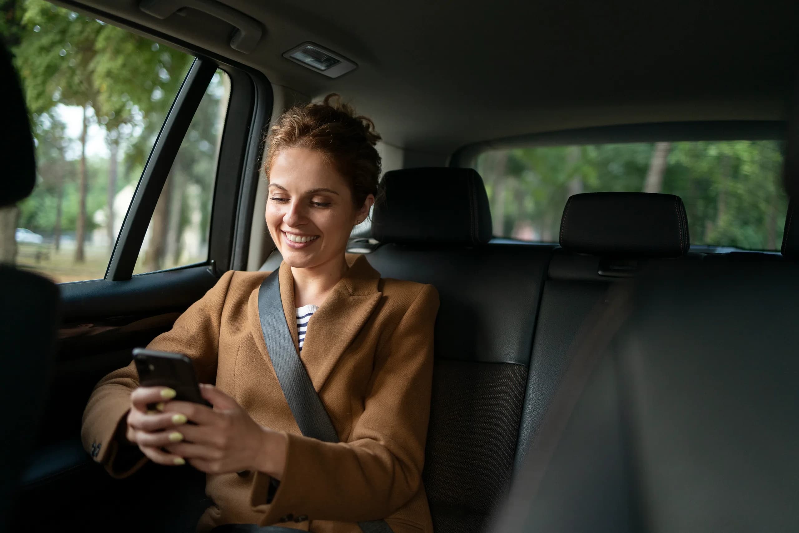Smiling woman checking her phone in the rear seat of a chauffeur-driven car