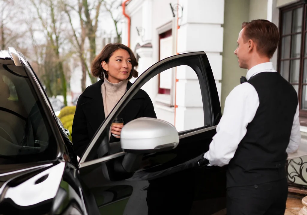 A chauffeur holding the car door open for a client outside a London hotel entrance