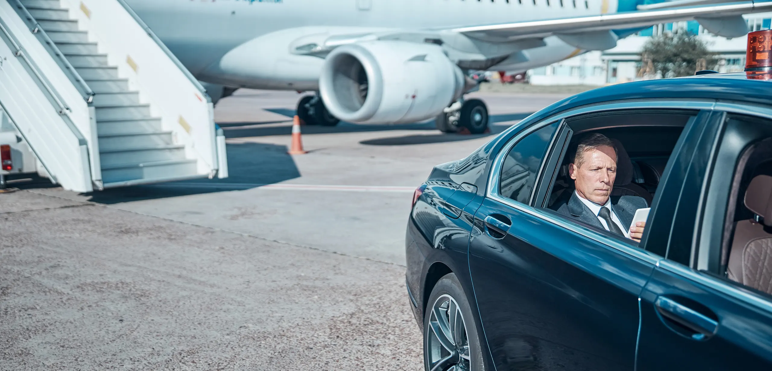 Executive reading on a tablet in the rear of a chauffeur-driven saloon beside aircraft steps on the tarmac