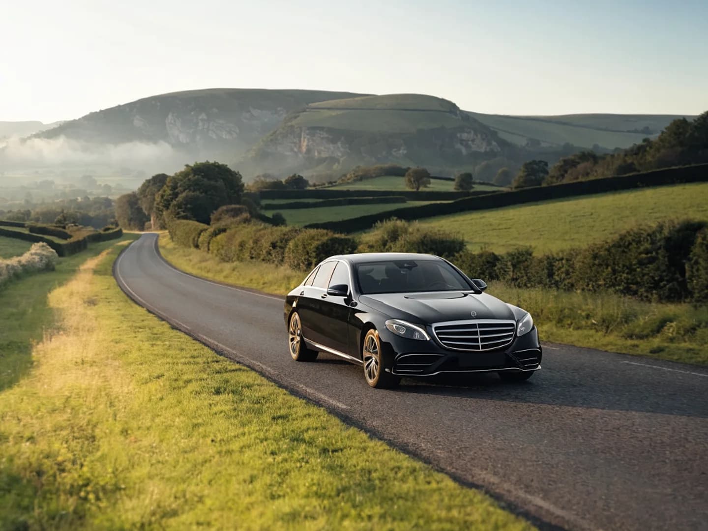 A black luxury saloon on a winding country road through rolling hills
