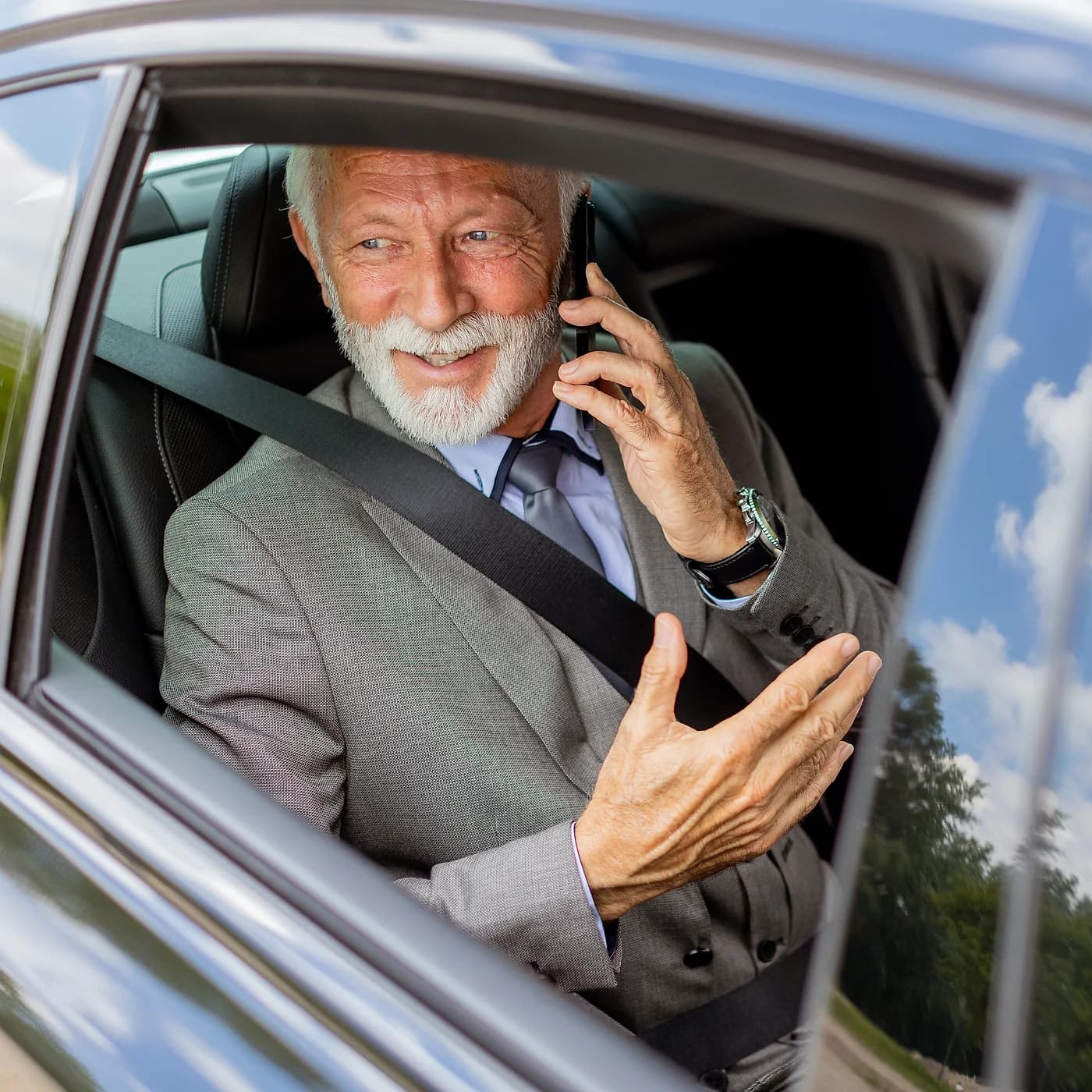 A senior business passenger taking a call from the rear seat of a chauffeur-driven car