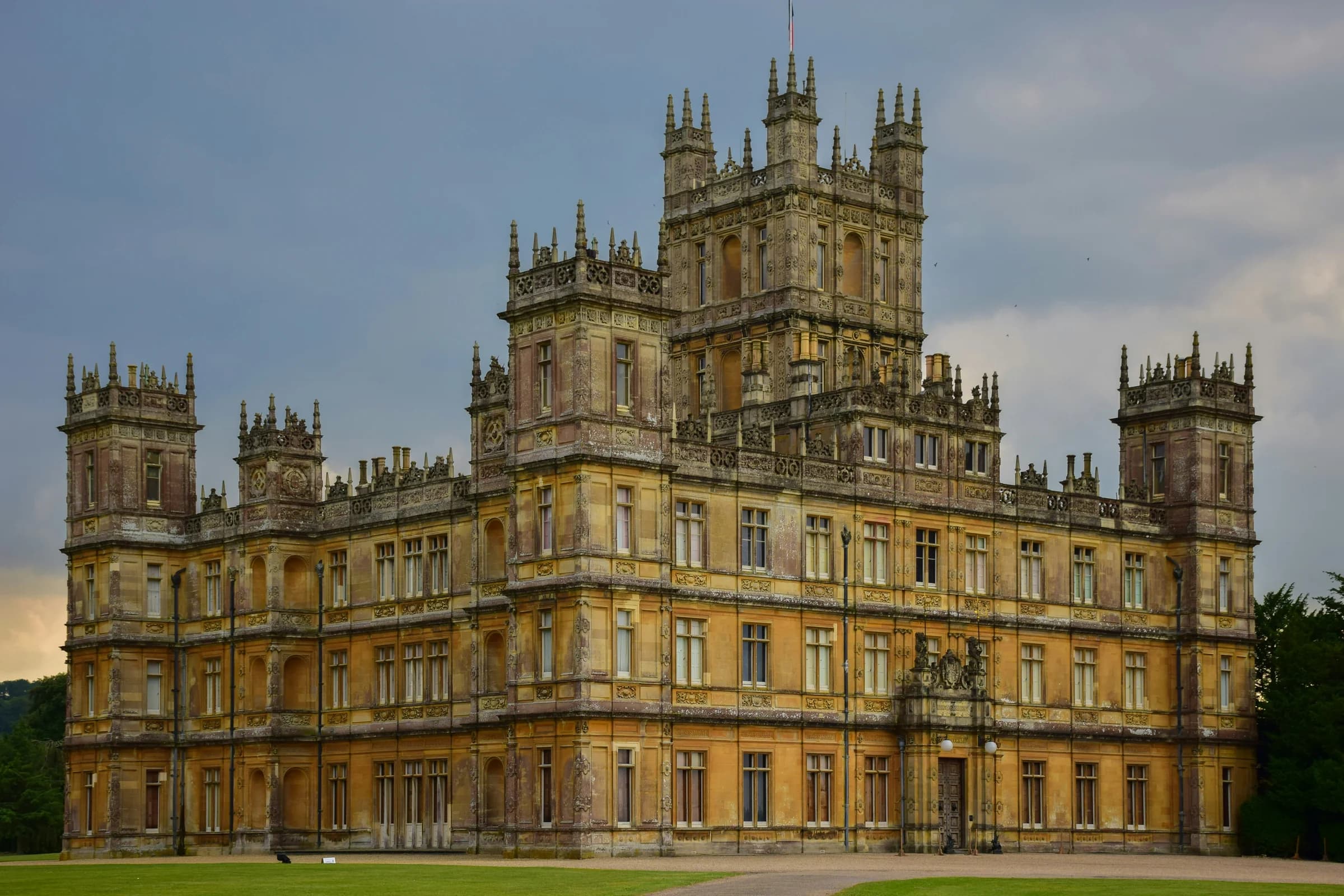 The front of Highclere Castle, its central tower and corner turrets under a grey summer sky