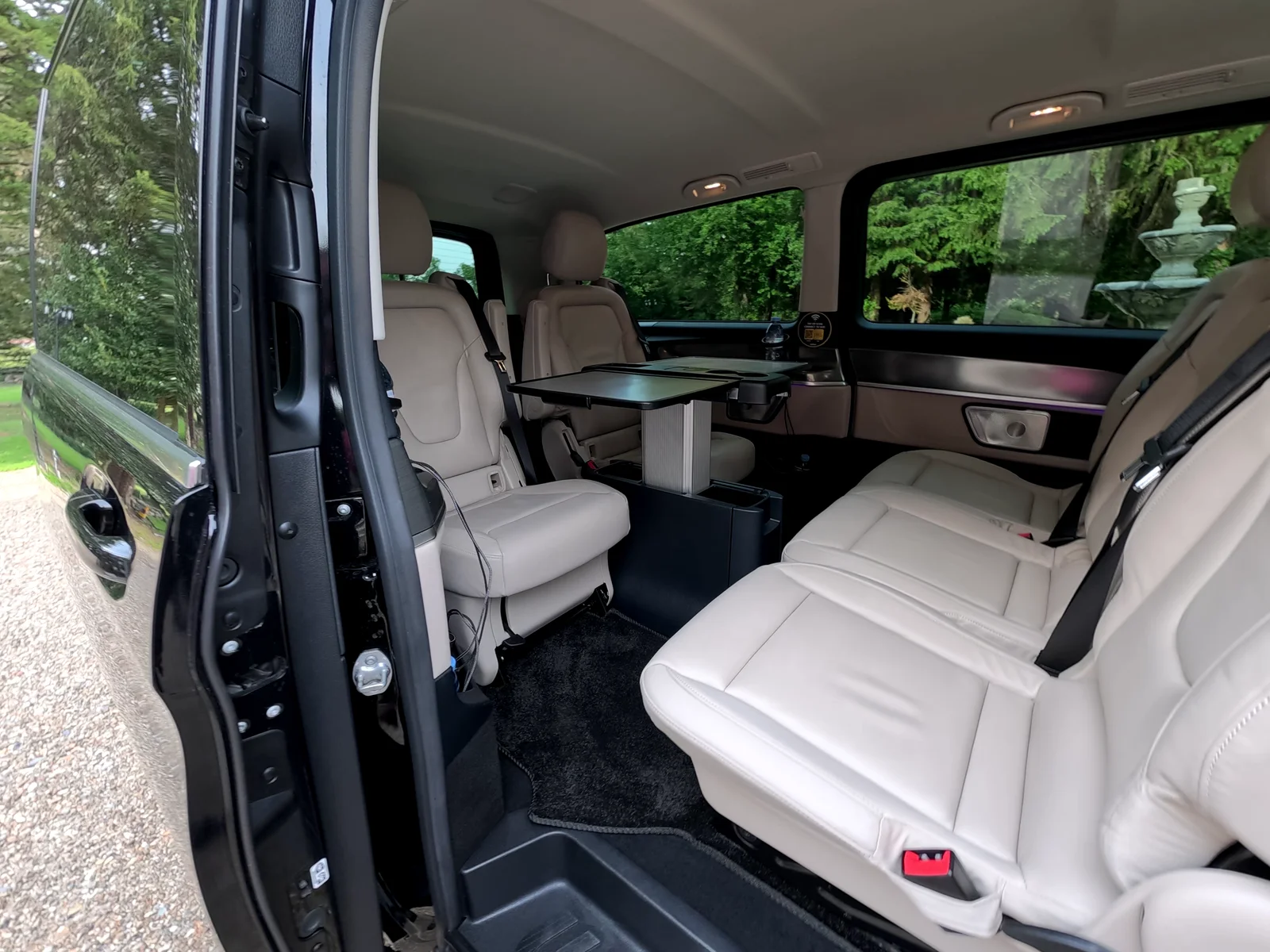 Open sliding door of a black Mercedes-Benz V-Class revealing cream leather conference seating and a folding work table