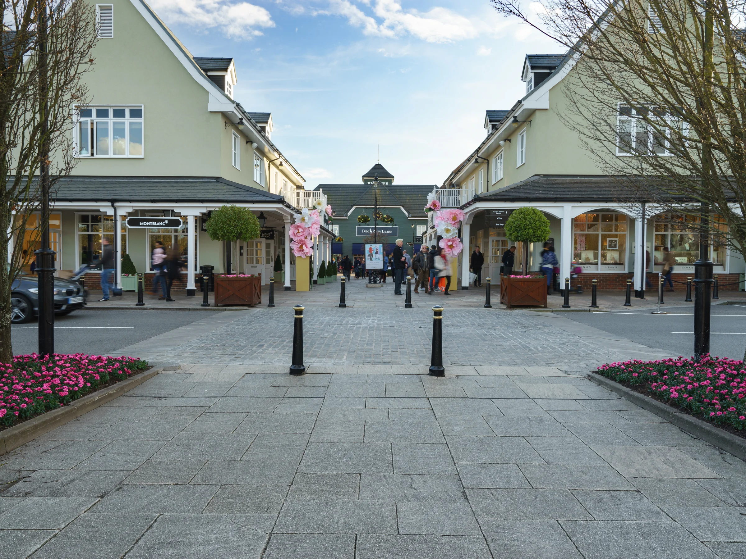 The pedestrian street at Bicester Village, lined with pale clapboard boutiques and planters of pink tulips