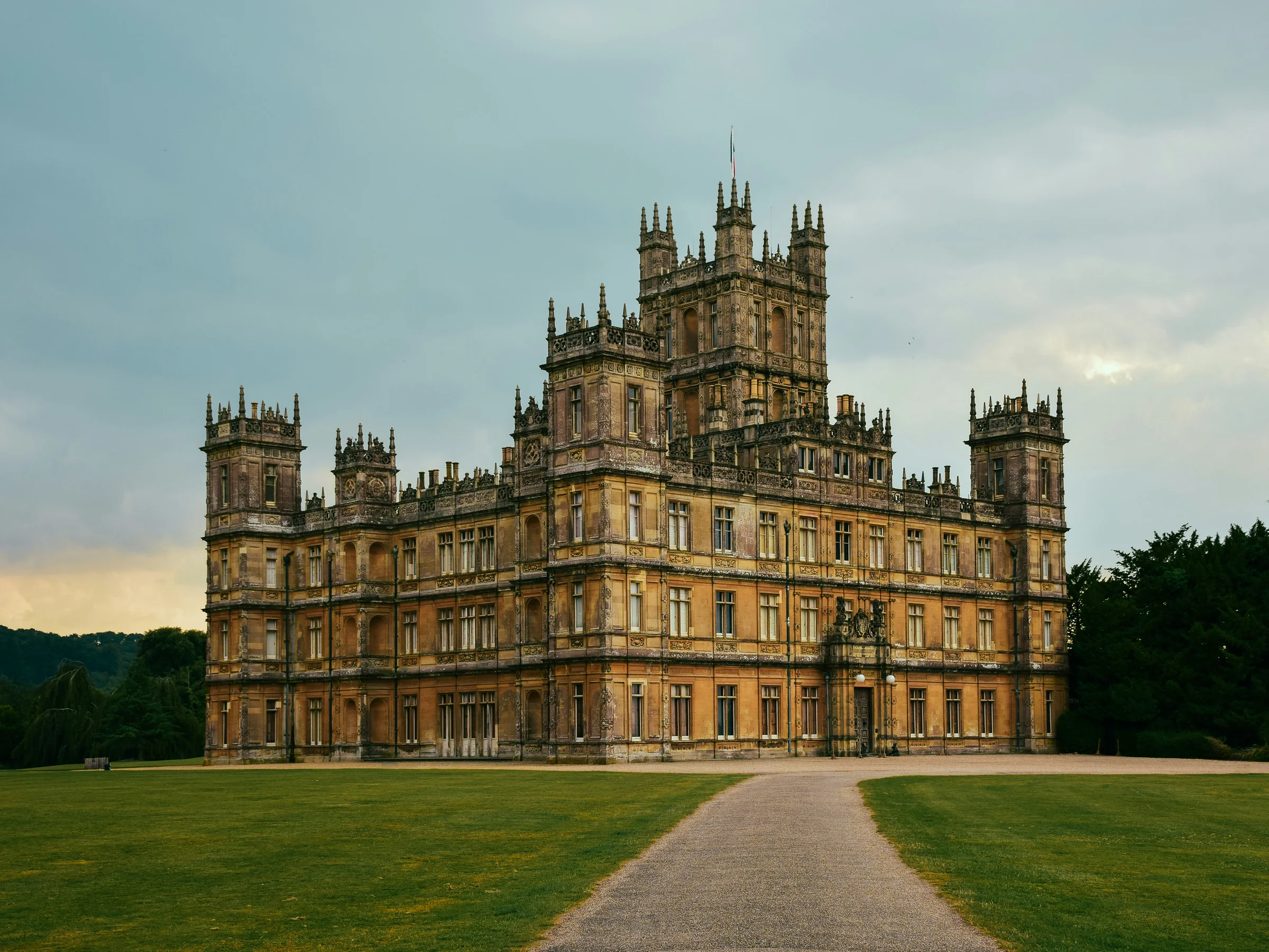 Highclere Castle's golden stone front and central tower seen across the lawn from the drive