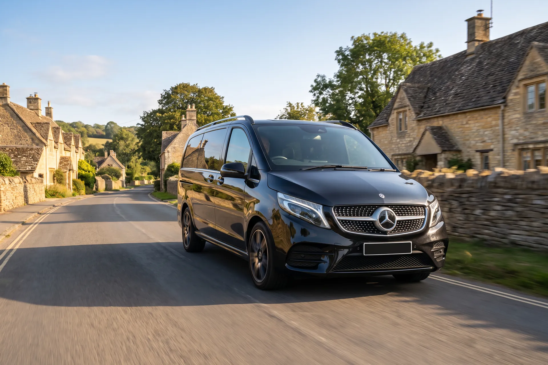 Black Mercedes-Benz V-Class on a country road between dry-stone walls and Cotswold stone cottages near Woodstock