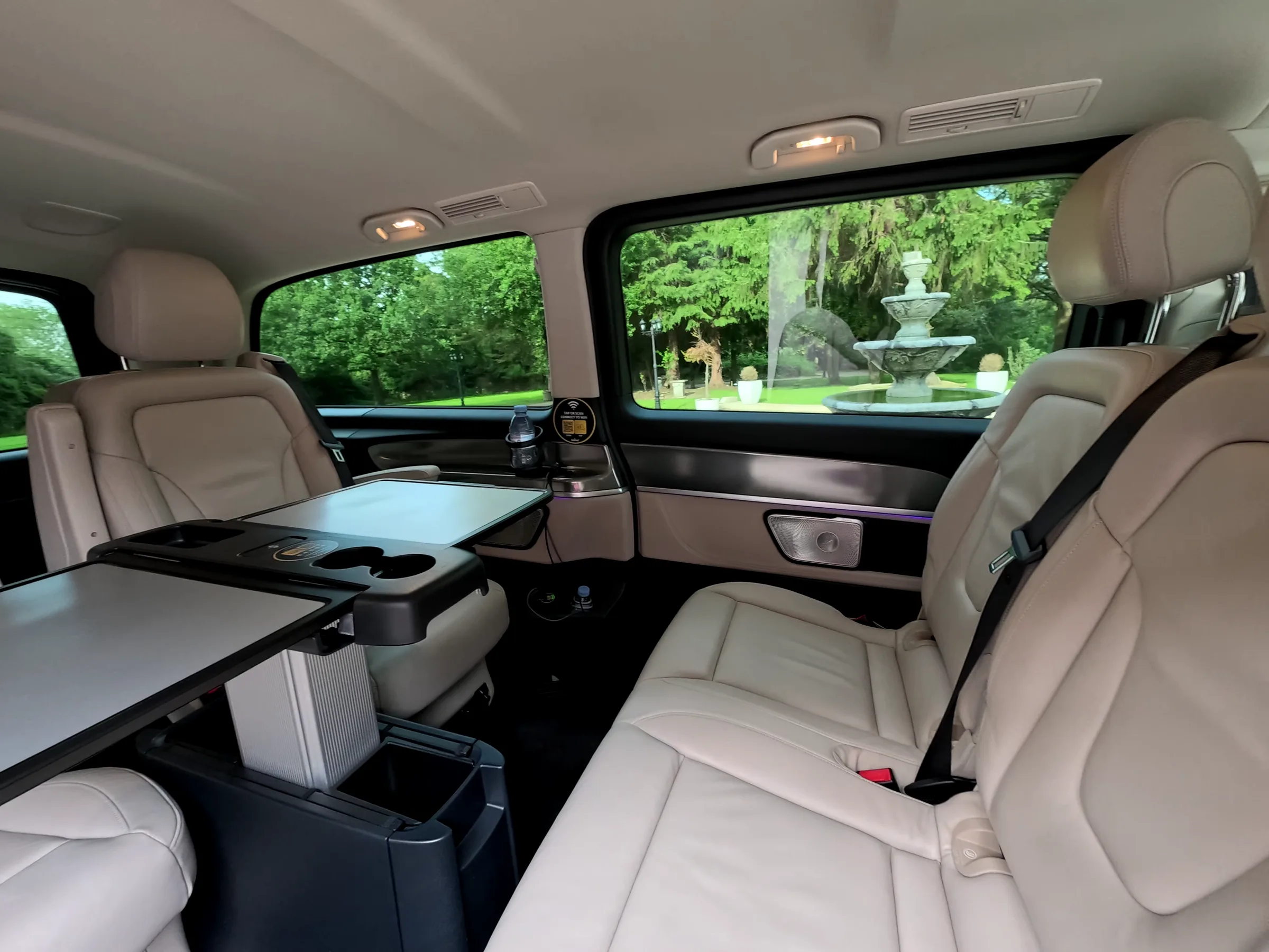The cream leather rear cabin of a DRVSTAR Mercedes V-Class, with folding tables deployed and chilled water ready