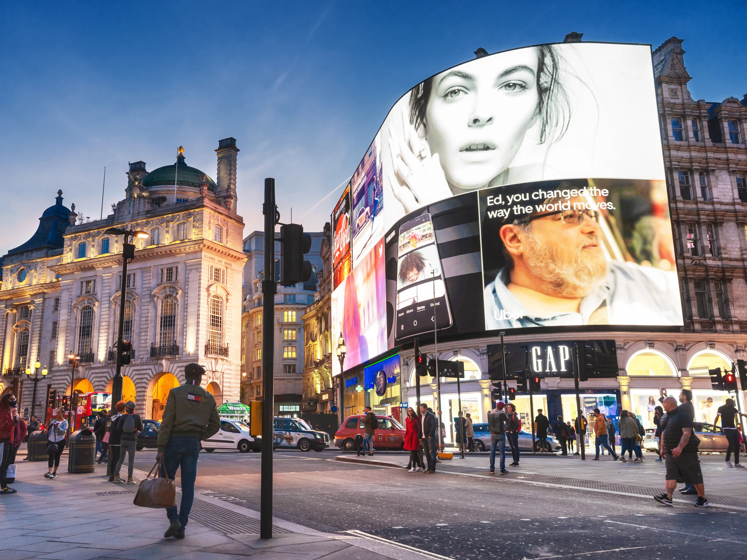 Piccadilly Circus at dusk, its curved screens lit above the evening crowds